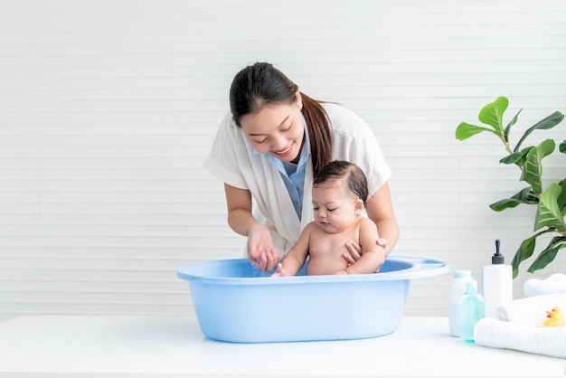 Mãe asiática dando banho em sua filha de 7 meses que o bebê sorrindo e feliz