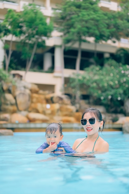 Mãe asiática e filho pequeno nadando em uma piscina nas férias de verão