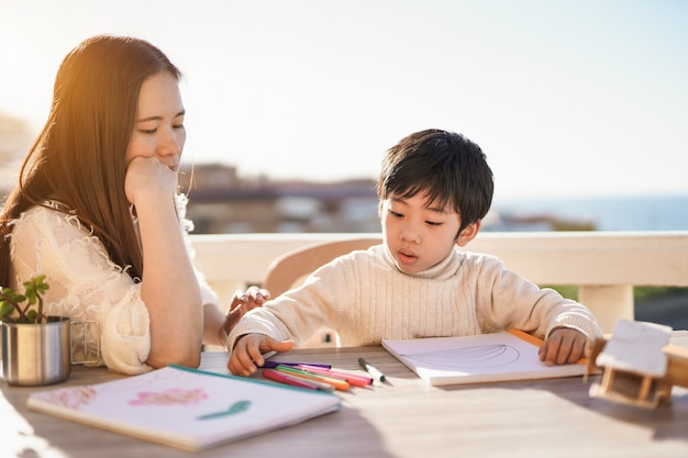 Mãe asiática fazendo atividades de desenho ao ar livre no pátio com o filho pequeno - Amor de mãe e filho