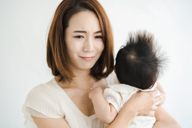Mãe asiática segurando um bebê e parecendo cansada