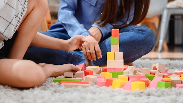 Mãe asiática trabalha em casa junto com o filho. Mãe e filho jogam bloco de madeira de cor. Criança criando brinquedo de construção. Estilo de vida da mulher e atividade familiar.