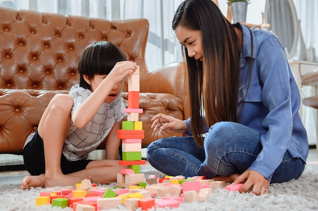 Mãe asiática trabalha em casa junto com o filho. mãe e filho jogam bloco de madeira de cor. criança criando brinquedo de construção. estilo de vida da mulher e atividade familiar.