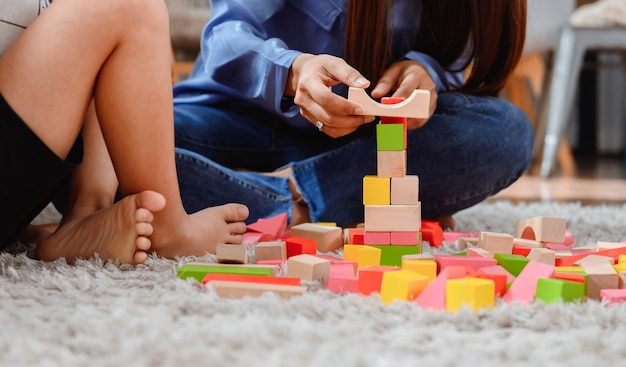 Mãe asiática trabalha em casa junto com o filho. Mãe e filho jogam bloco de madeira de cor. Criança criando brinquedo de construção. Estilo de vida da mulher e atividade familiar.