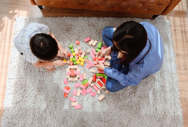 Mãe asiática trabalha em casa junto com o filho. Mãe e filho jogam bloco de madeira de cor. Criança criando brinquedo de construção. Estilo de vida da mulher e atividade familiar.