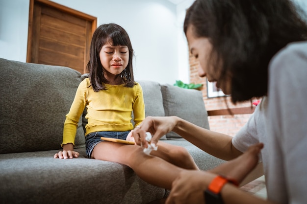 Mãe asiática tratando filha ferida com anti-séptico em casa