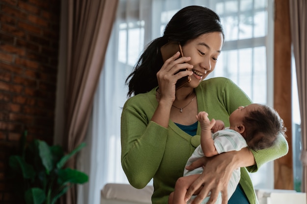 Mãe asiática usando smartphone ao segurar a filha pequena