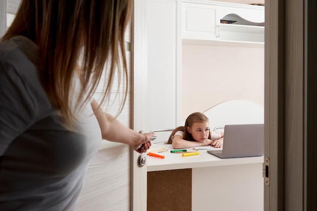 Mãe assistindo sua filha triste fazendo lição de casa no laptop em casa