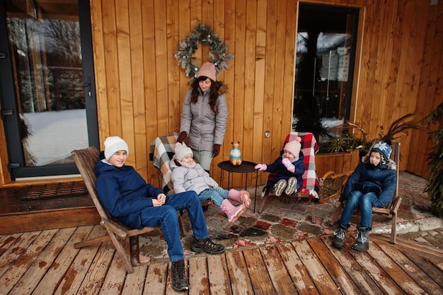 Mãe atraente com seus quatro filhos no terraço de uma casa de madeira em dia de inverno