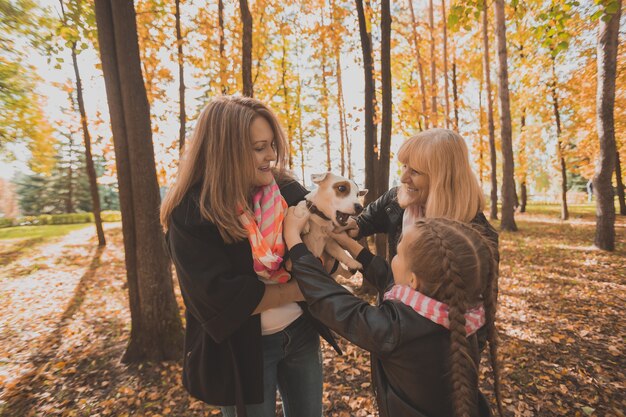 Mãe, avó e filha segura jack russell terrier e brinca com ele no outono lá fora. Animal de estimação e conceito de família
