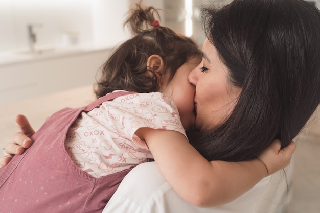 Mãe beija a filha dela. Filha e mãe abraçam gentilmente.