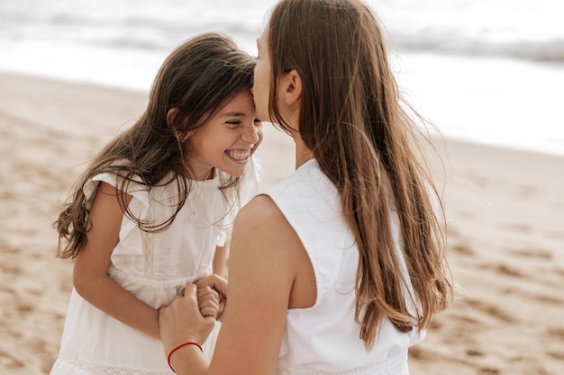 Mãe beijando a testa da filha sorridente na praia