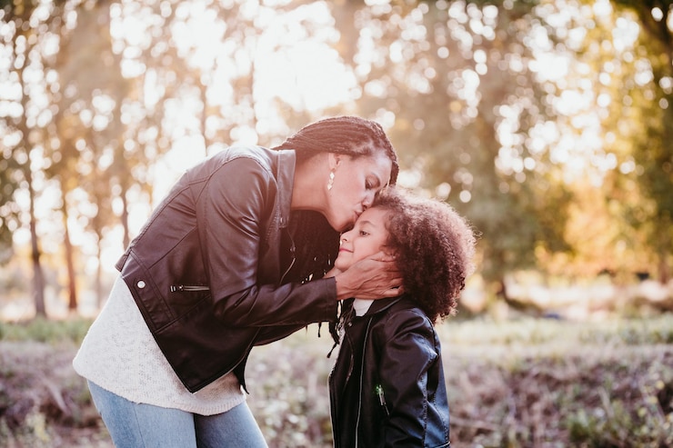 Foto mãe beijando filha enquanto está de pé contra as árvores