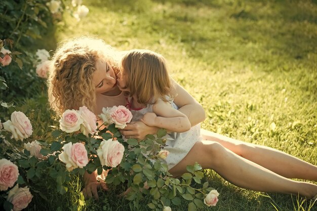 Mãe beijando filha na grama verde em dia ensolarado de verão