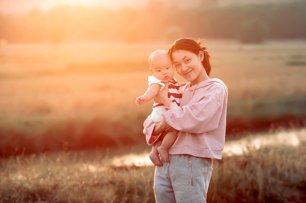 Mãe biológica segurando um bebê de 4 meses dê um passeio pelos campos de arroz ao pôr do sol