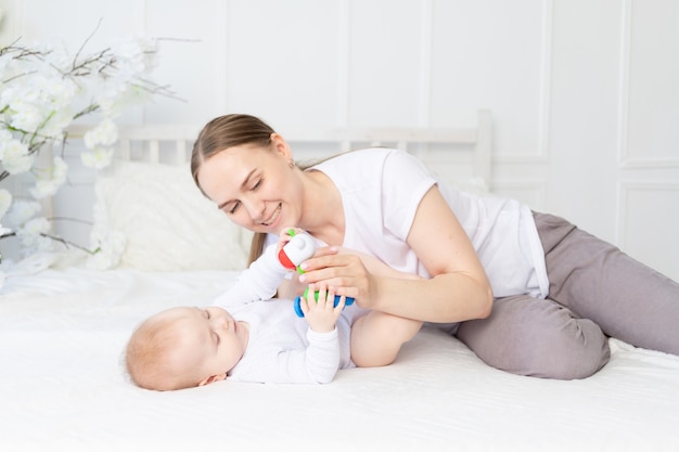 Mãe brinca com chocalho de bebê na cama branca em casa.