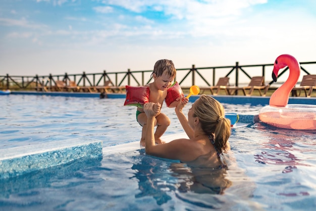 Mãe brinca com seu filho com mangas na piscina no verão