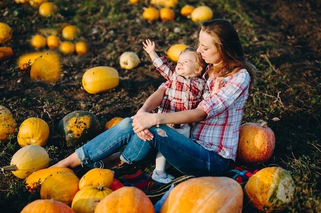 Mãe brincando com a filha em um campo com abóboras, véspera de Halloween