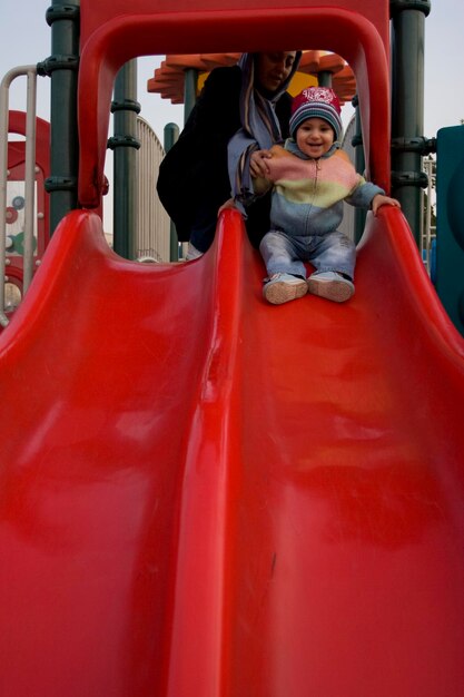 Foto mãe brincando com o filho no escorregador no playground