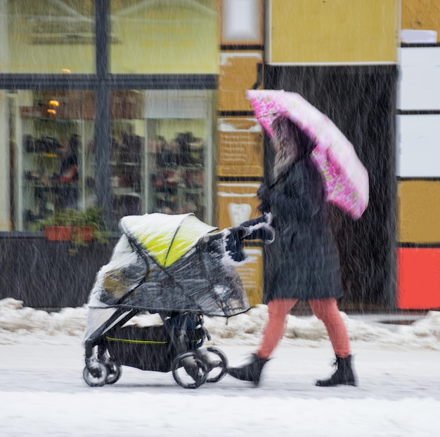 Mãe caminha com a criança no carrinho em um dia de inverno nevado. Desfoque de movimento intencional. Imagem desfocada