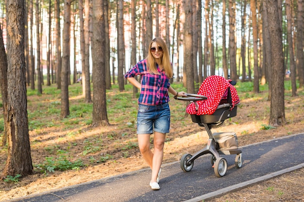 Mãe caminhando enquanto empurra um carrinho de bebê no parque.