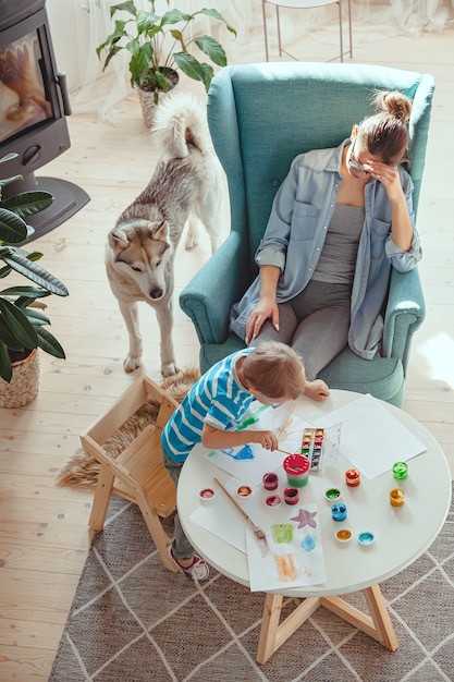 Mãe cansada e criança com autismo pintando aquarela juntas em