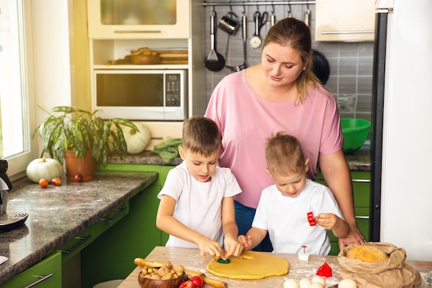 Mãe carinhosa ajuda filhos em idade pré-escolar a preparar biscoitos, mãe sorridente e amorosa aprendem a cozinhar com os filhos pequenos, fazendo almoço juntos na cozinha no fim de semana