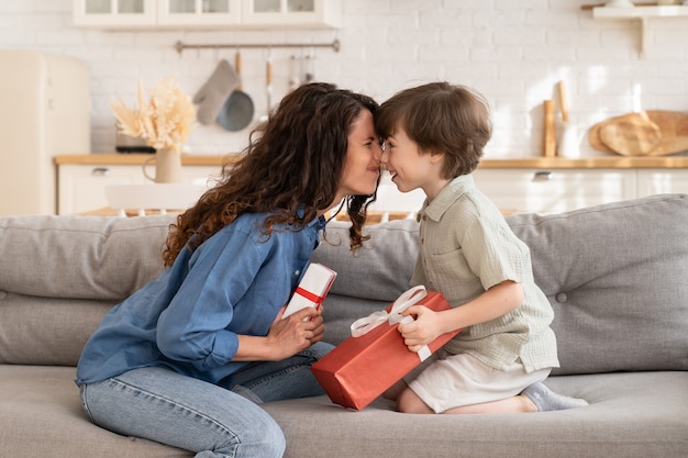 Foto mãe carinhosa e filho sentados juntos no sofá segurando um presente, mãe e adorável criança trocando presentes