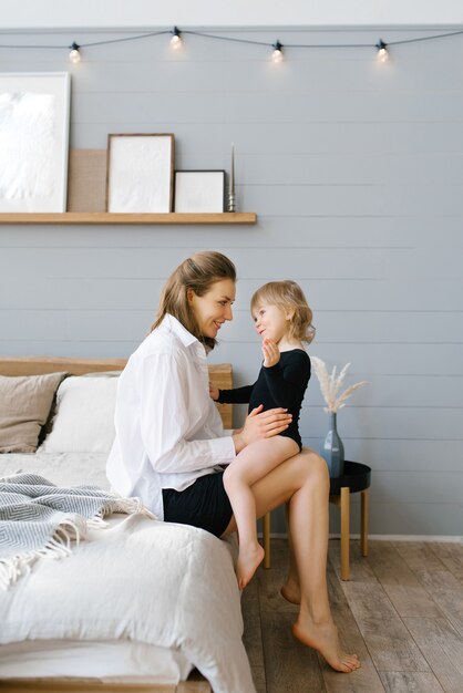 Mãe carinhosa e linda filha sentadas na cama em casa