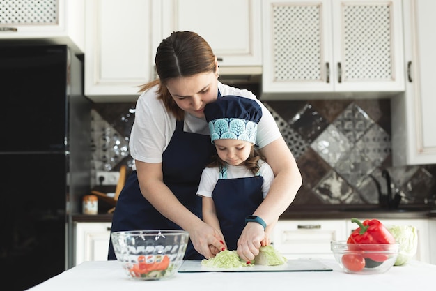 Mãe carinhosa ensinando a filha a cozinhar salada na cozinha