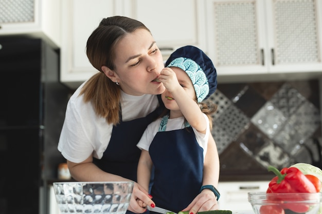 Mãe carinhosa ensinando filha a cozinhar salada na cozinha