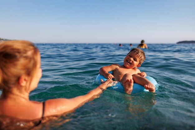 Mãe carinhosa monta seu filho em um anel inflável no mar