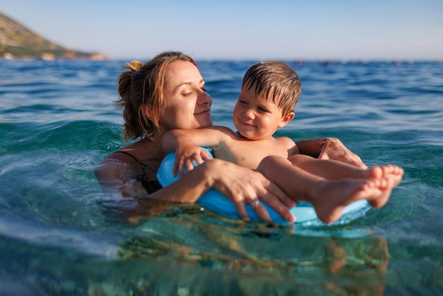 Mãe carinhosa monta seu filho em um anel inflável no mar