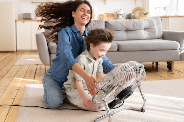 Mãe carinhosa relaxa e se diverte com a criança em casa sente-se rindo junto com o filho em frente ao ventilador