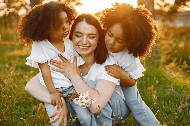 Mãe caucasiana e duas filhas afro-americanas se abraçando ao ar livre