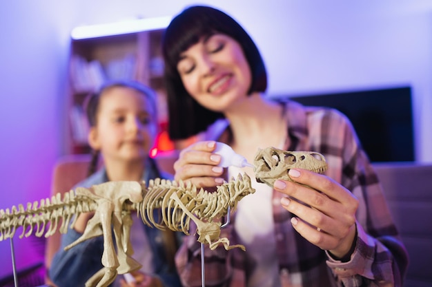 Mãe caucasiana monta esqueleto de dinossauro com filha inteligente e bonita