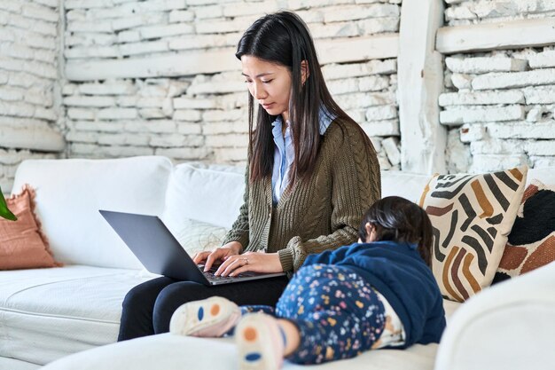 Mãe chinesa equilibra o trabalho no laptop e o tempo com a criança no sofá