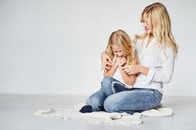 Mãe com a filha dela está no chão do estúdio com fundo branco.