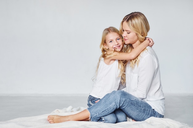 Mãe com a filha dela está no chão do estúdio com fundo branco.