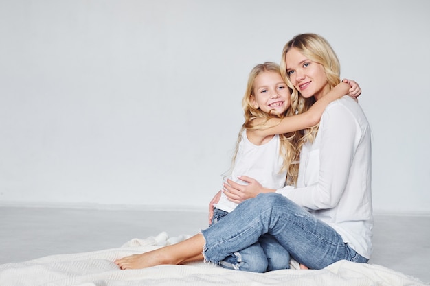 Mãe com a filha dela está no chão do estúdio com fundo branco.