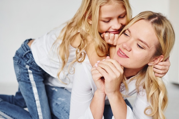 Mãe com a filha junto no estúdio com fundo branco.