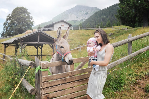 Mãe com a filha se divertindo no rancho da fazenda e conhecendo um burro Conceito de terapia de animais de estimação no campo com burro na fazenda educacional Conceito de terapia de animais de estimação com crianças