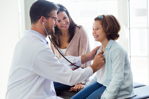 Foto mãe com a filha sendo examinada com estetoscópio por pediatra.