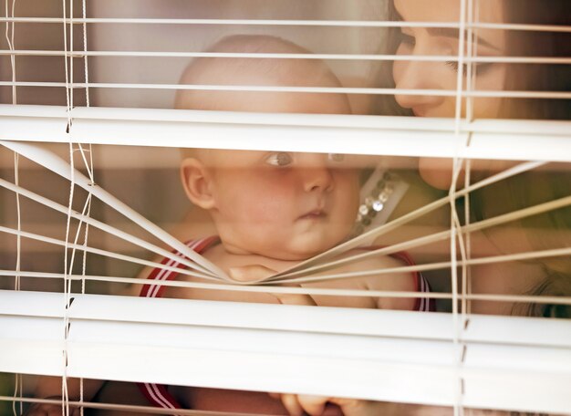 Mãe com bebê olhando através das cortinas