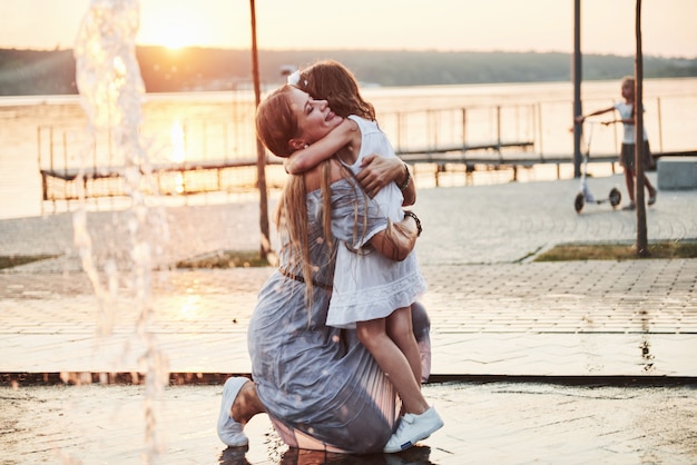 Mãe com bebê perto da fonte ao pôr do sol