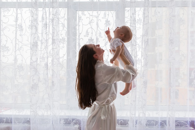 mãe com bebê perto da janela do quarto