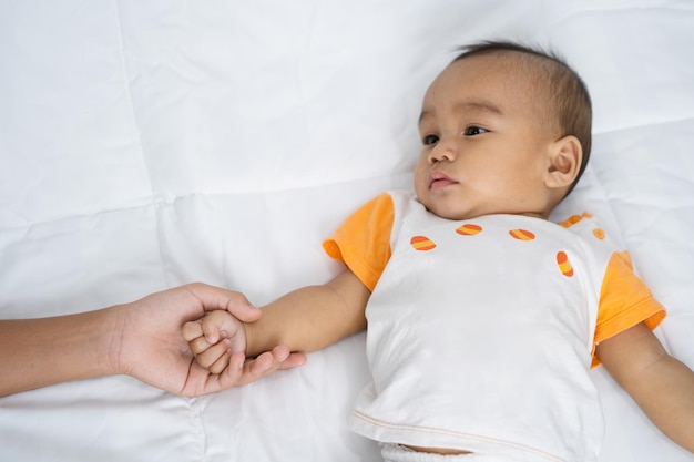 Mãe com bebê segurando a mão no colchão branco