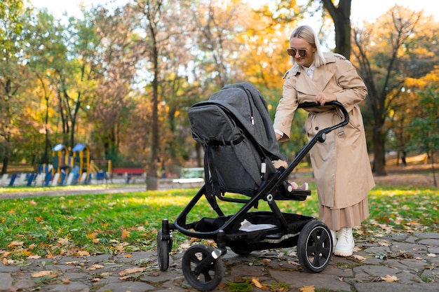 Mãe com carrinho de bebê caminhando no parque outono