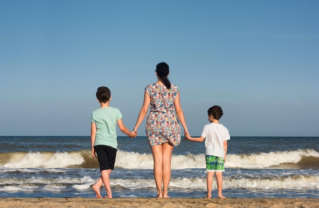 Mãe com dois filhos na praia olhando para o mar