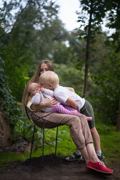 Mãe com dois filhos sentados na cadeira no fundo da natureza. Quadro vertical.