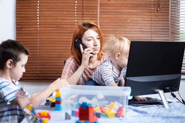 Mãe com dois meninos de joelhos tenta rir em casa.